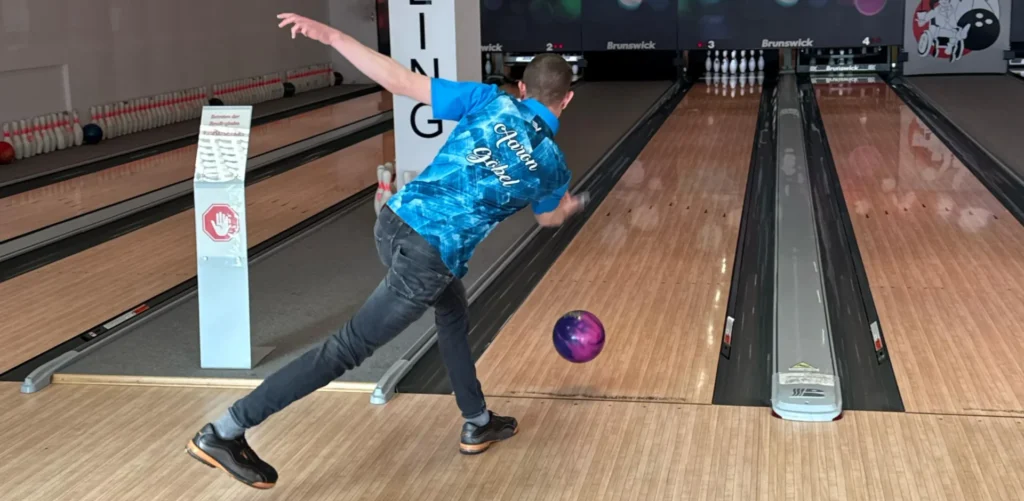 Bowler beim Wurf mit violetter Bowlingkugel auf gepflegter Bahn in moderner Bowlinghalle
